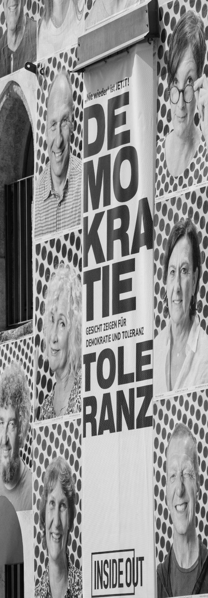 InsideOut Installation Wandinstallation mit Porträtfotos und zentralem Plakat mit den Worten ‚DEMOKRATIE‘ und ‚TOLERANZ‘.